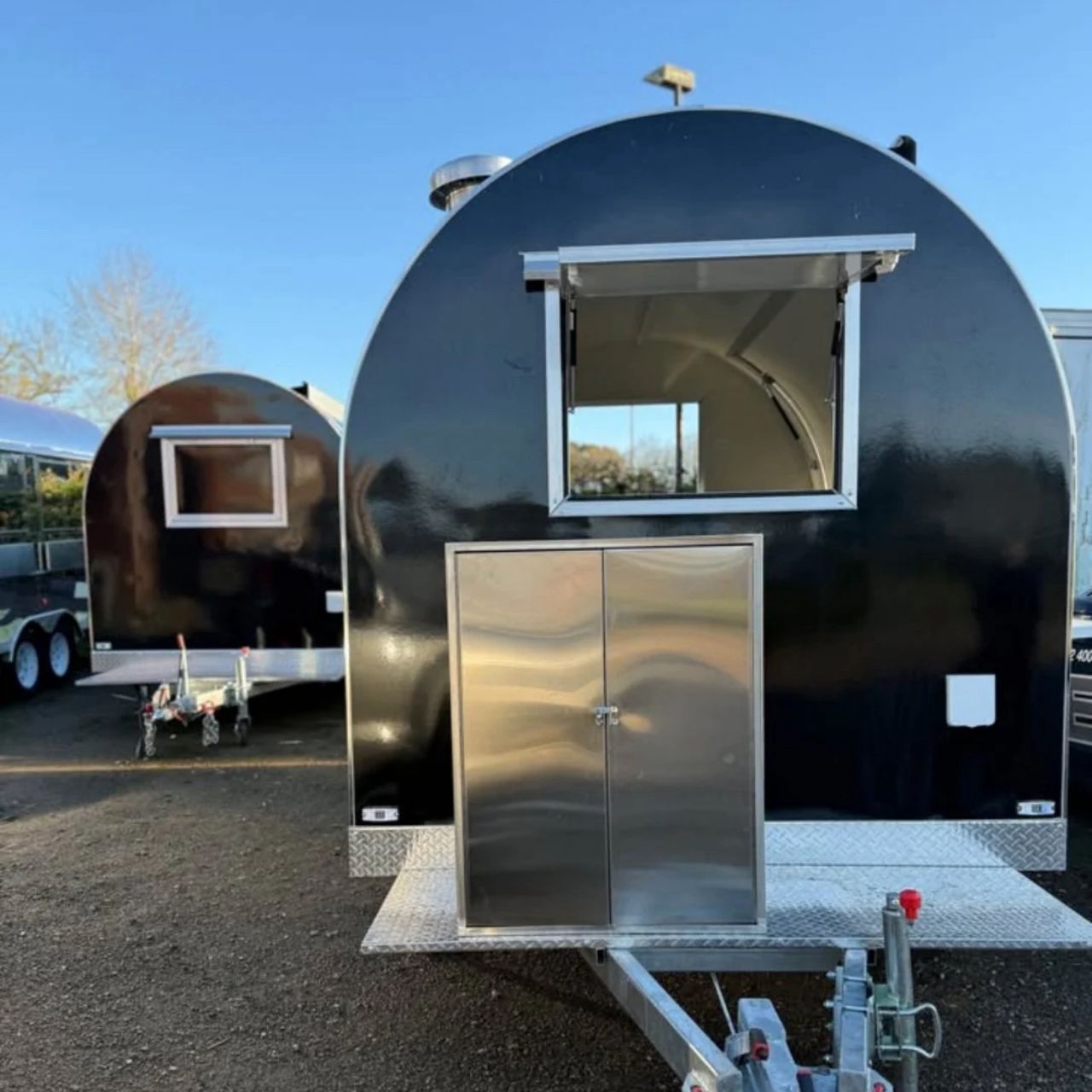 IMG-20260519-WA0014 - Glossy black teardrop trailer with a large open window and a front metal storage cabinet on a gravel lot.