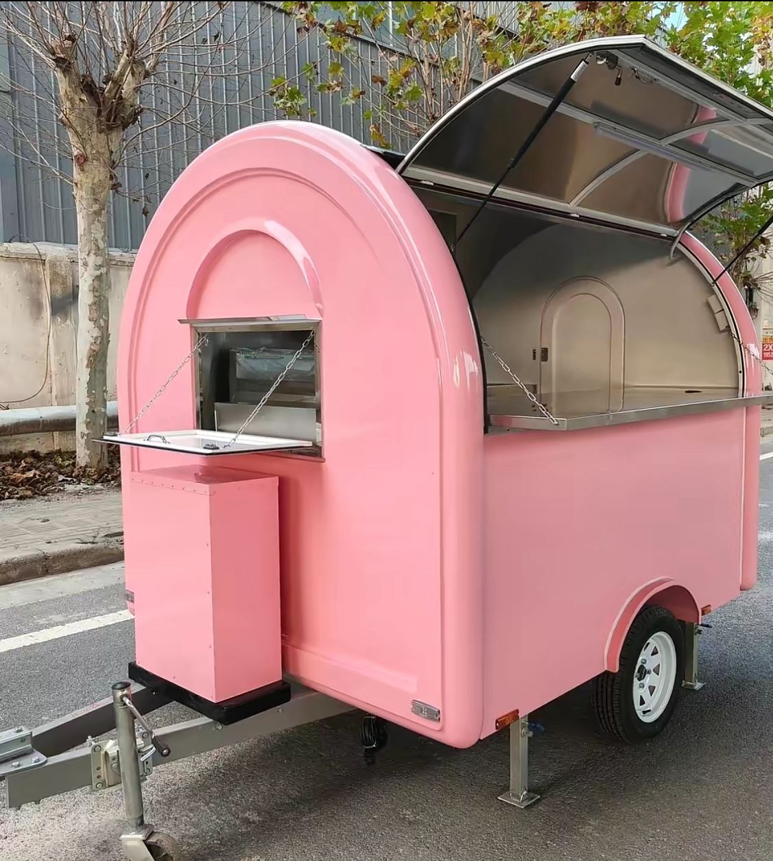 IMG-20260519-WA0016 - Pink vintage-style food trailer with a curved top and open service window on a street, showing a small pink front counter.