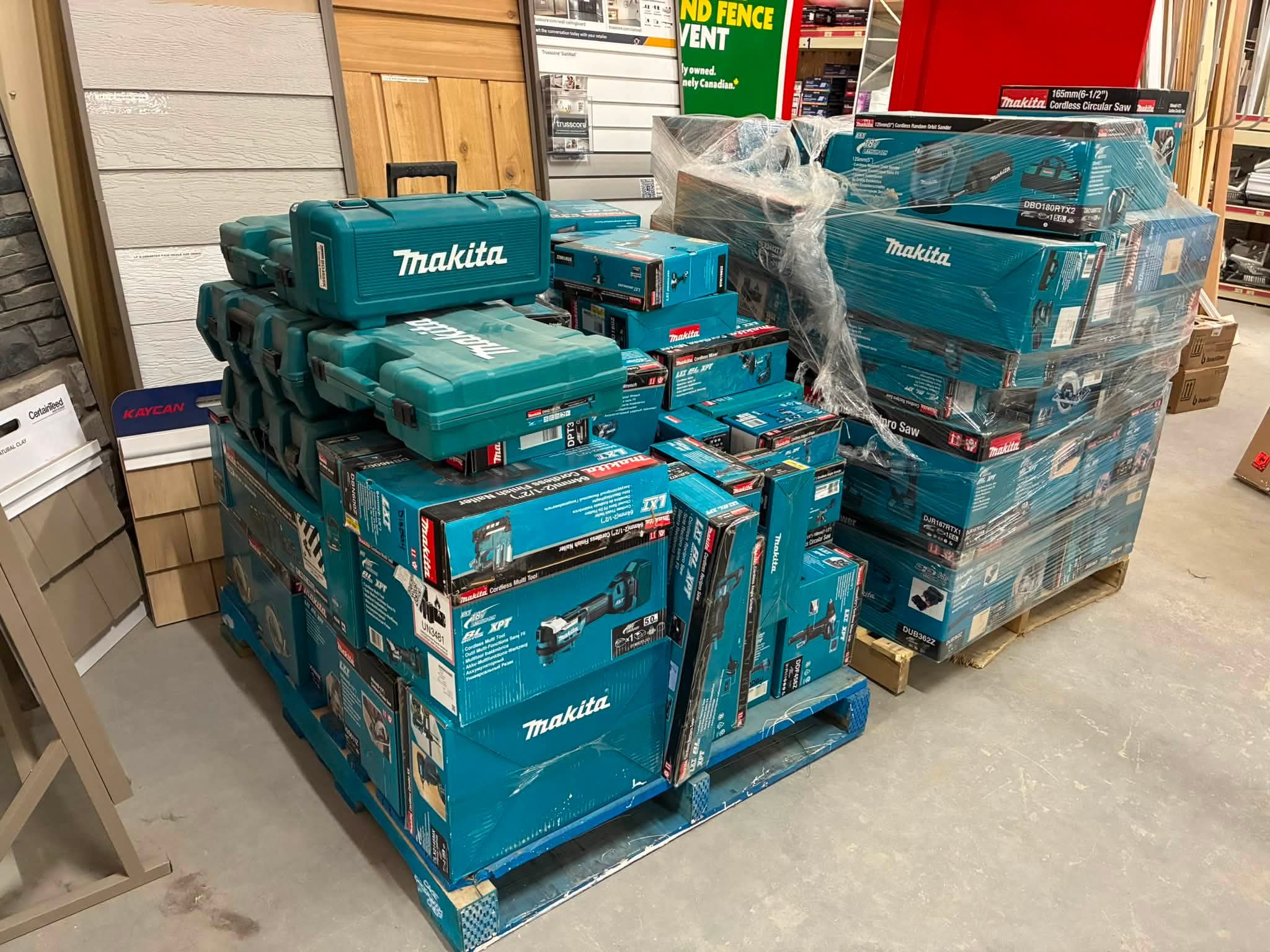 Stacks of blue Makita tool boxes on a pallet in a hardware store, wrapped in plastic with shelving and signage in the background